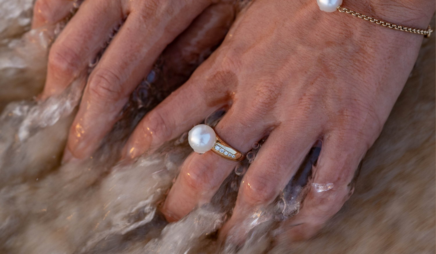 A pair of hands in the water at Cygnet Bay Pearl Farm. The person wears a beautiful pearl ring featuring a South Sea pearl complemented by adiamonds set into a gold band.