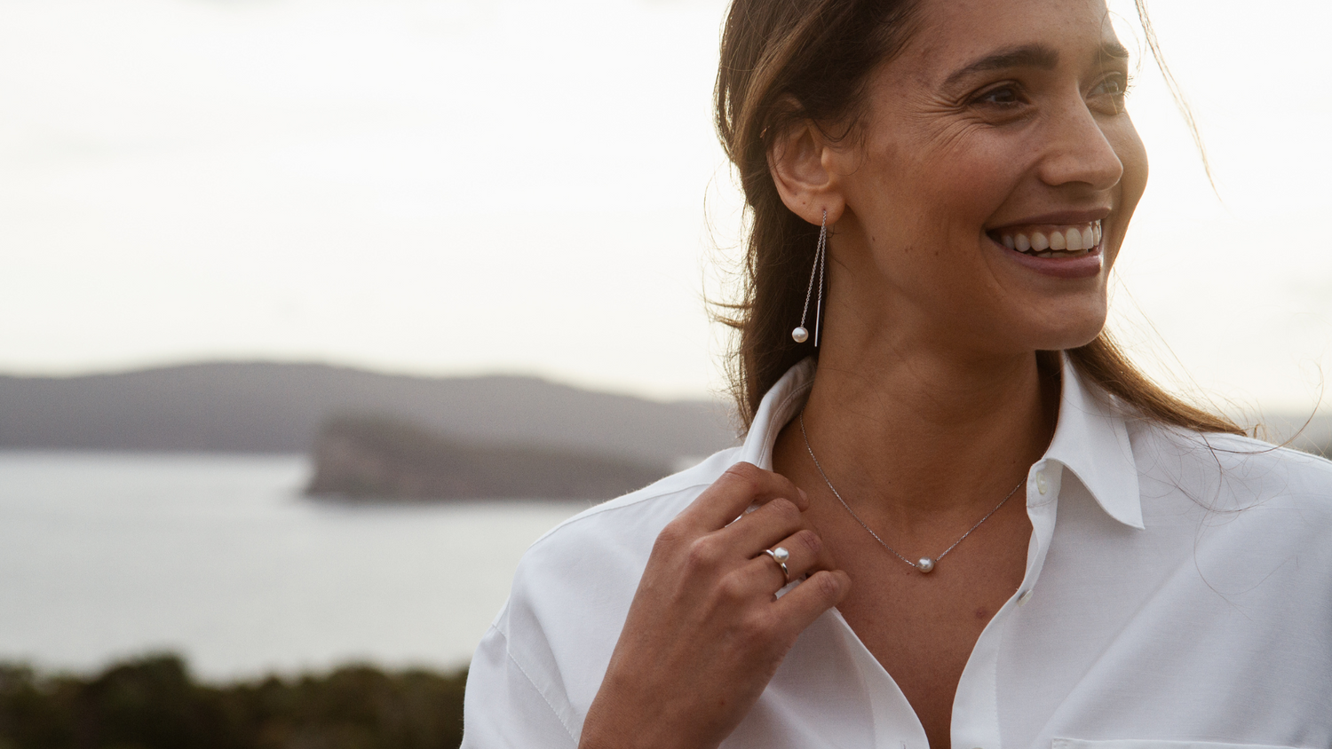 A woman wears her stunning Savanna pearl jewellery collection which features our Australian Akoya set in a pair of thread through earrings, and matching necklace.