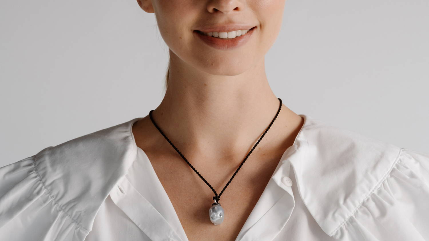 A woman wears her beautiful baroque pearl pendant set alongside beautiful black diamonds hung on a silk cord rope.