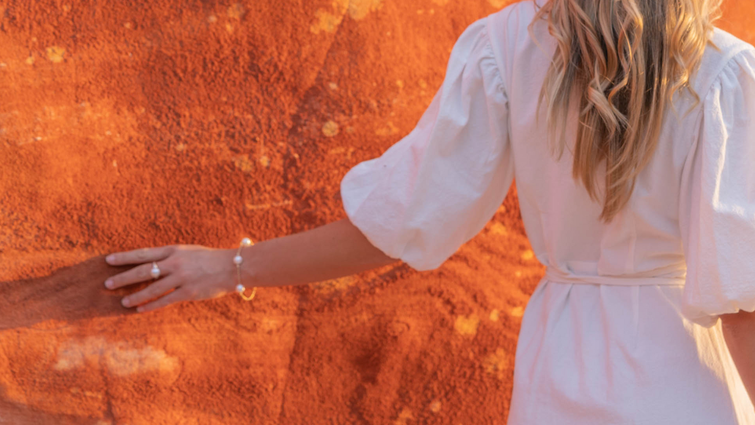 A woman brushes her hand against the vibrant pindan local to the Kimberley, where our stunning Australian South Sea pearls are born.