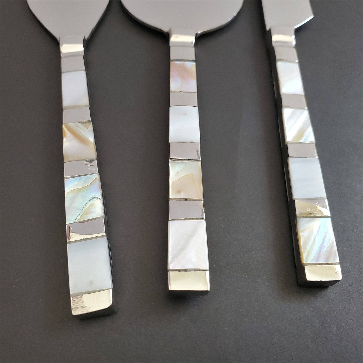 Set of three cheese knives with decorative mother of pearl handles on a dark background
