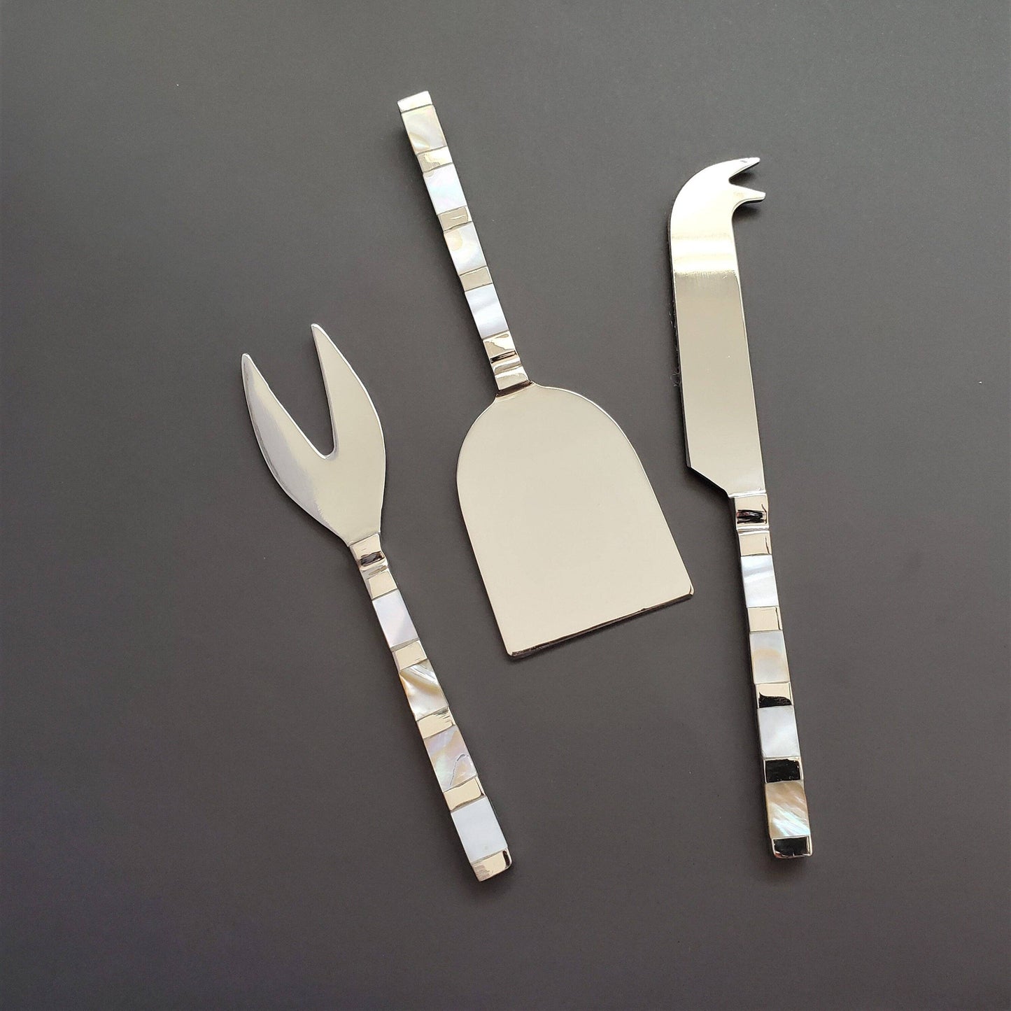 Set of three silver cheese knives on a dark gray background