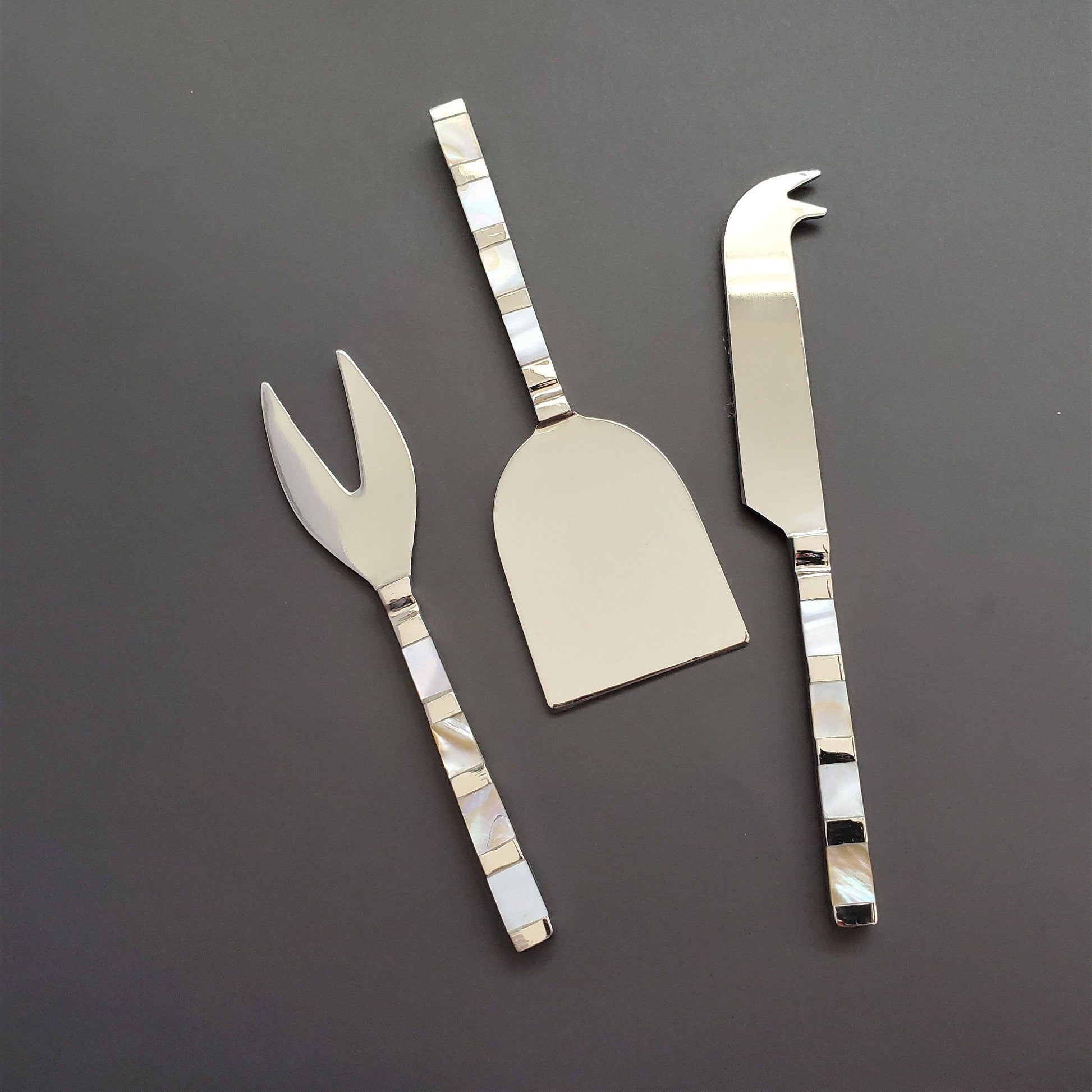 Set of three silver cheese knives on a dark gray background