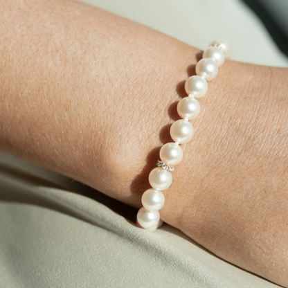 A woman wears her striking Pearl Strand Diamond Rondel Bracelet features twenty-four (24) 6.5mm Round AAA grade Broken Bay (NSW) grown Australian Akoya pearls. This 18cm pearl strand is complimented by 33 White Diamonds, set with an 18ct Yellow Gold clasp.