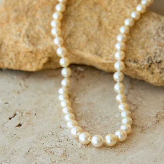 Pearl strand necklace on a sandy surface with rocks in the background