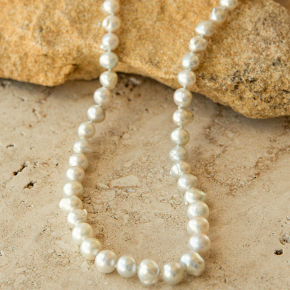 Pearl strand necklace on a sandy surface with rocks in the background