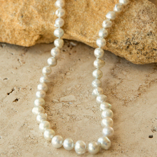 Pearl strand necklace on a sandy surface with rocks in the background