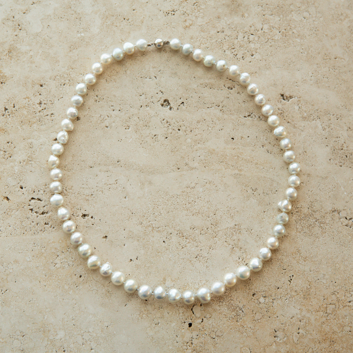 Pearl strand necklace on a textured beige surface