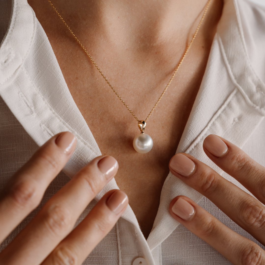 A woman wears her gorgeous white, Australian South Sea pearl set on a gold pendant and hung on a gold chain. This pearl shines with its natural lustre.