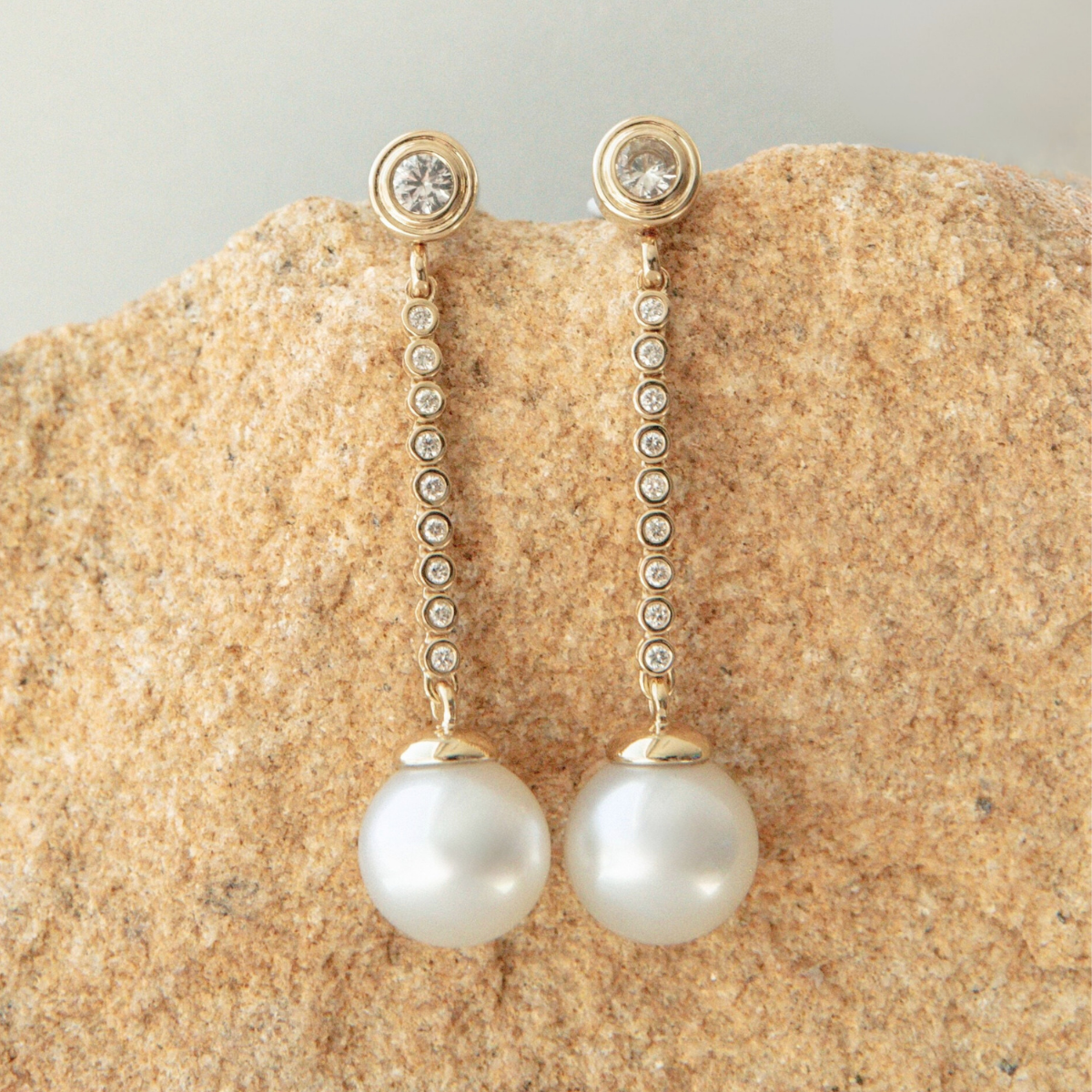 Pearl and diamond earrings on a textured beige surface