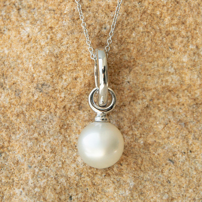 Pearl pendant on a white gold chain against a beige sandstone background
