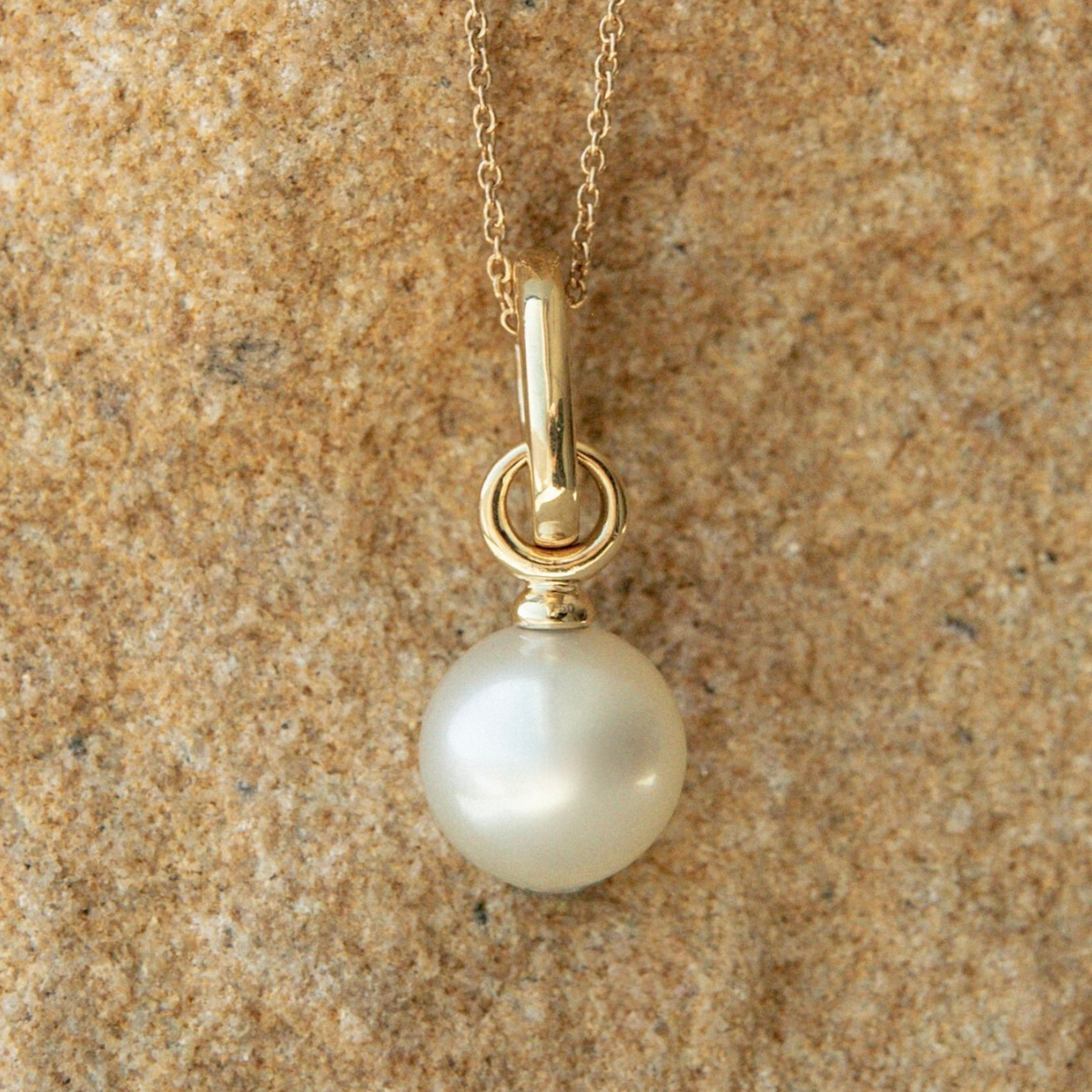 Pearl pendant on a gold chain against a beige stone background