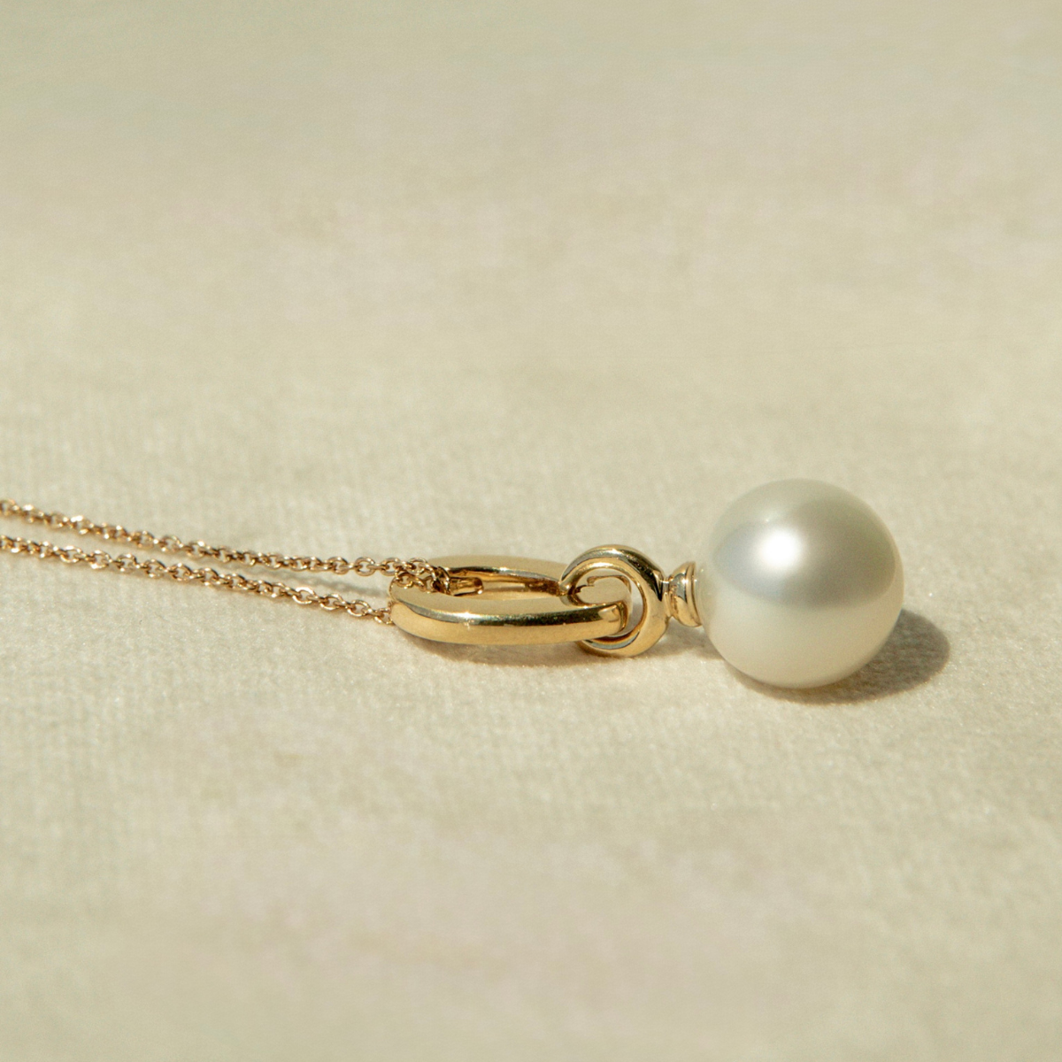 Gold necklace with a pearl pendant on a beige background