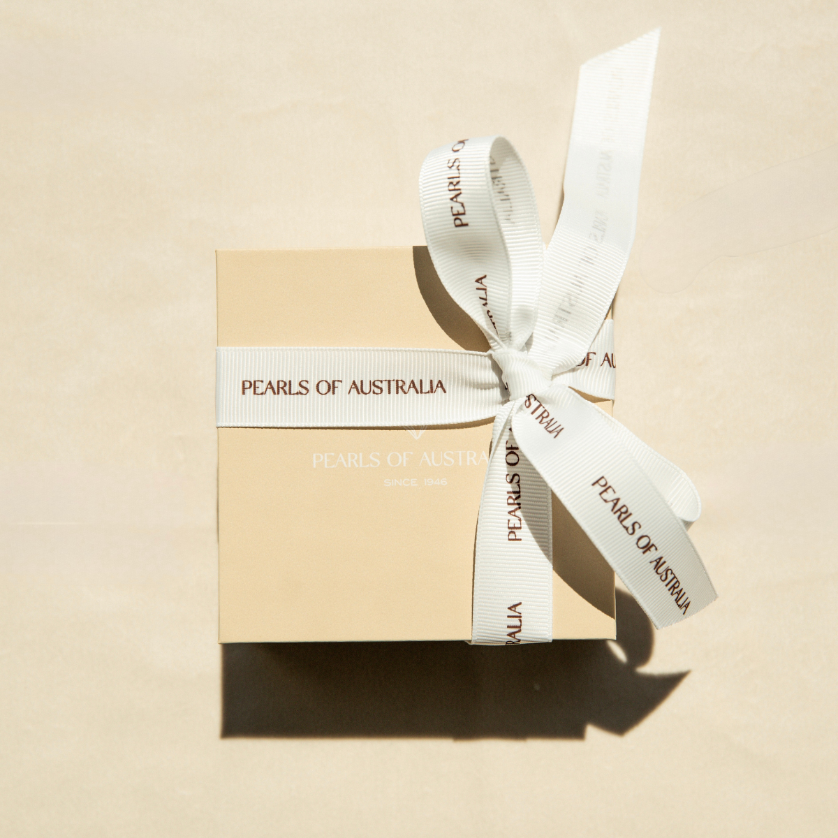 Gift box with a white ribbon labeled 'Pearls of Australia' on a beige background