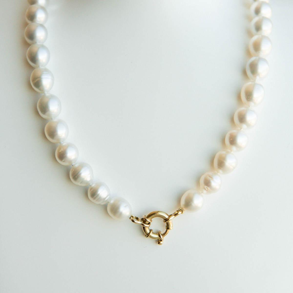 Pearl strand necklace with a gold bolt clasp on a textured beige surface