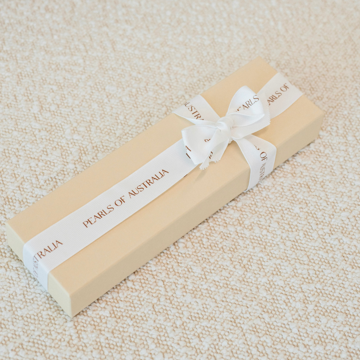 Beige pearl bracelet gift box with white ribbon and 'Pearls of Australia' label on a textured beige surface