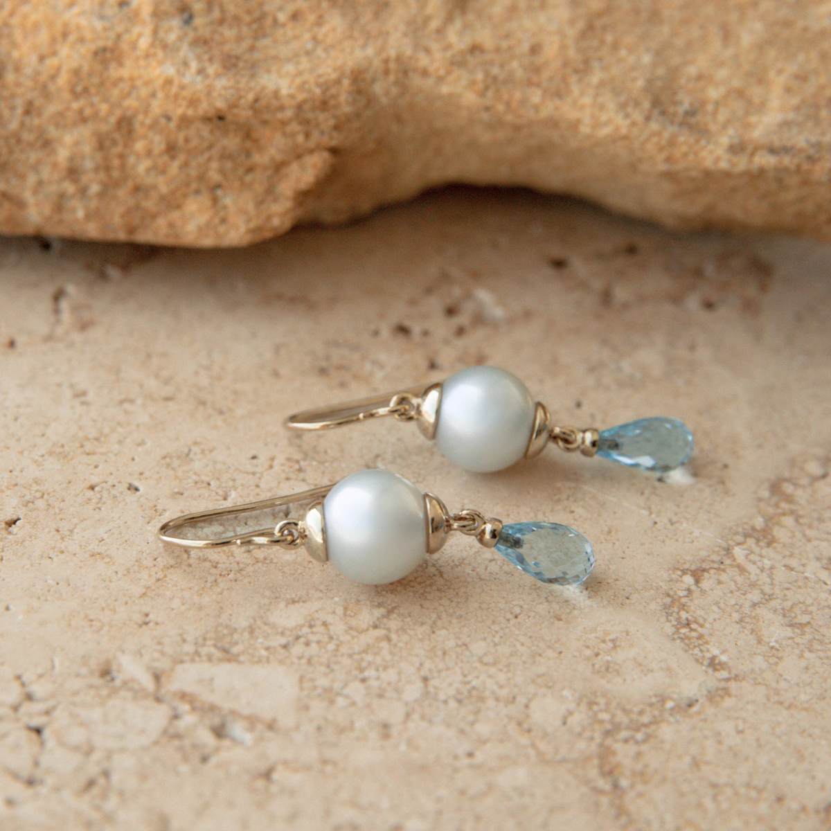 Pearl and blue gemstone earrings on a stone surface
