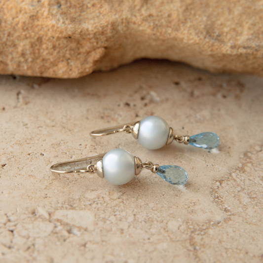 Pearl and blue gemstone earrings on a stone surface