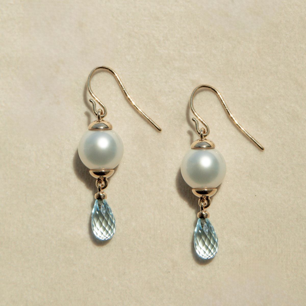 Pair of pearl and blue gemstone earrings on a beige background