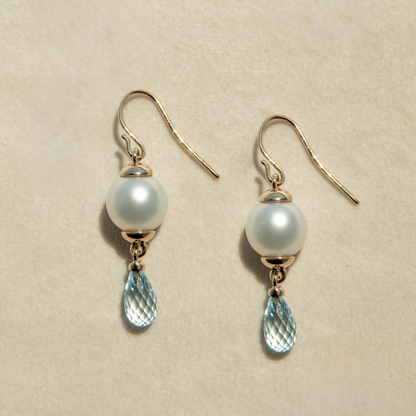 Pair of pearl and blue gemstone earrings on a beige background