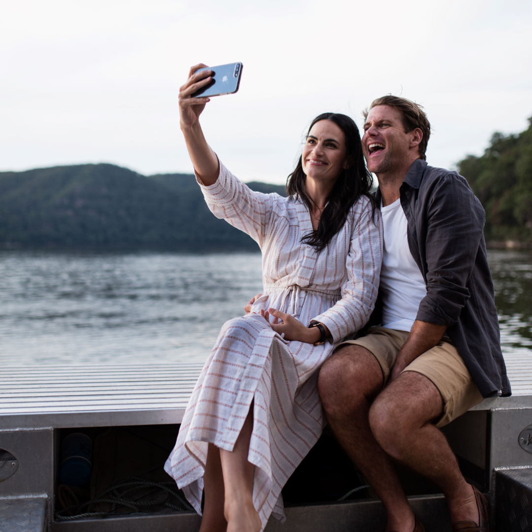 A couple smile widely during their Broken Bay pearl farm tour, as they enjoy the stunning sites of the Hawkesbury River at sunset.