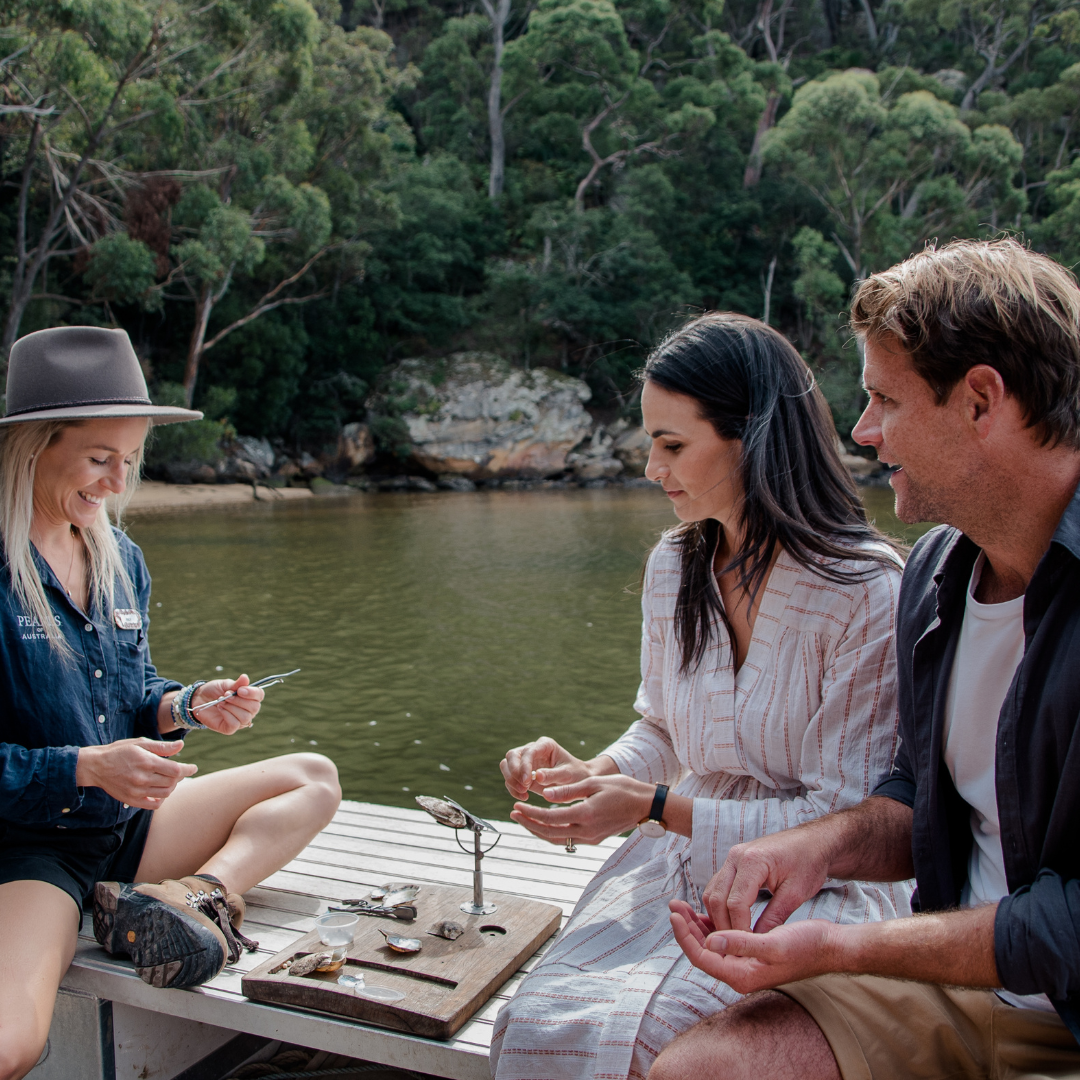 A tour guide shows her guests the life cycle of our Australian Akoya pearls during a Farm Cruise tour that takes place on the Hawkesbury River in New South Wales. The couple watch the tour guide intently as they hold stunning Akoya pearls in their hands.