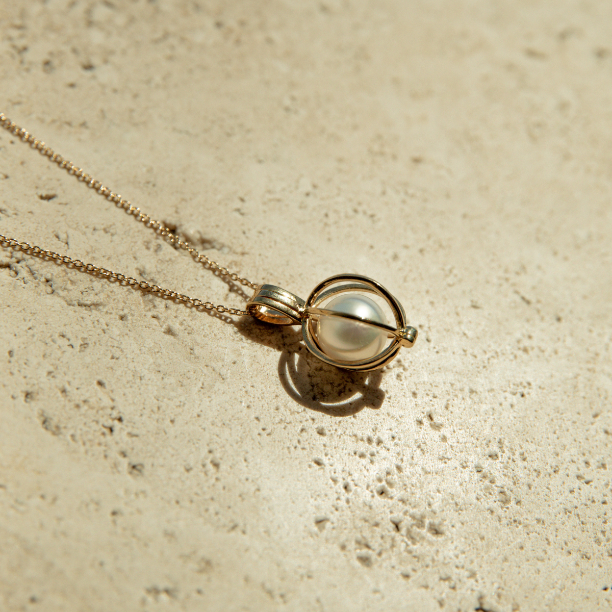 Gold necklace with a pearl cage pendant on a textured beige surface