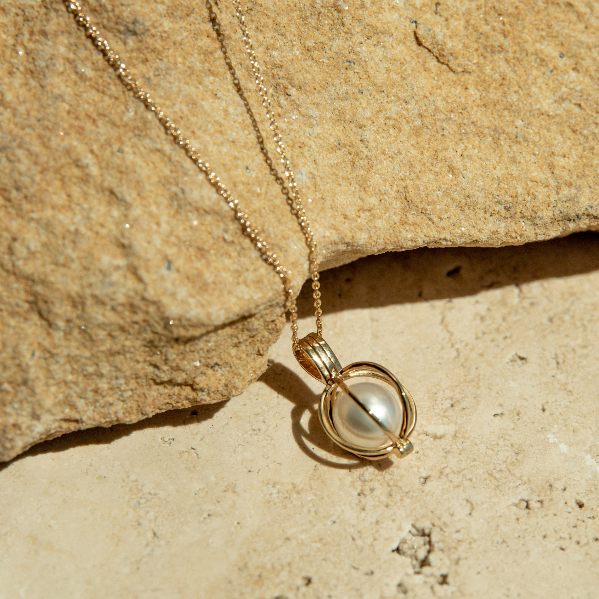Gold necklace with a pearl cage pendant on a textured beige surface