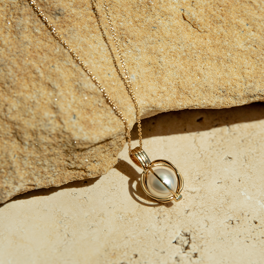 Gold necklace with a pearl cage pendant on a textured beige surface