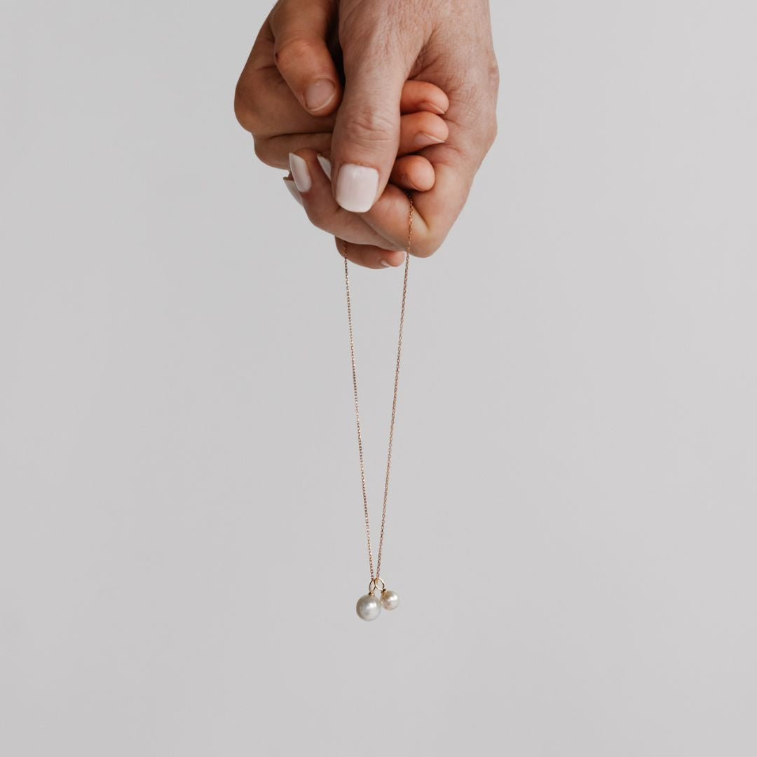 A mother and daughter hold hands, while holding a Charm Pearl Set that features both an Akoya and South Sea pearl charm hung on a gold chain.