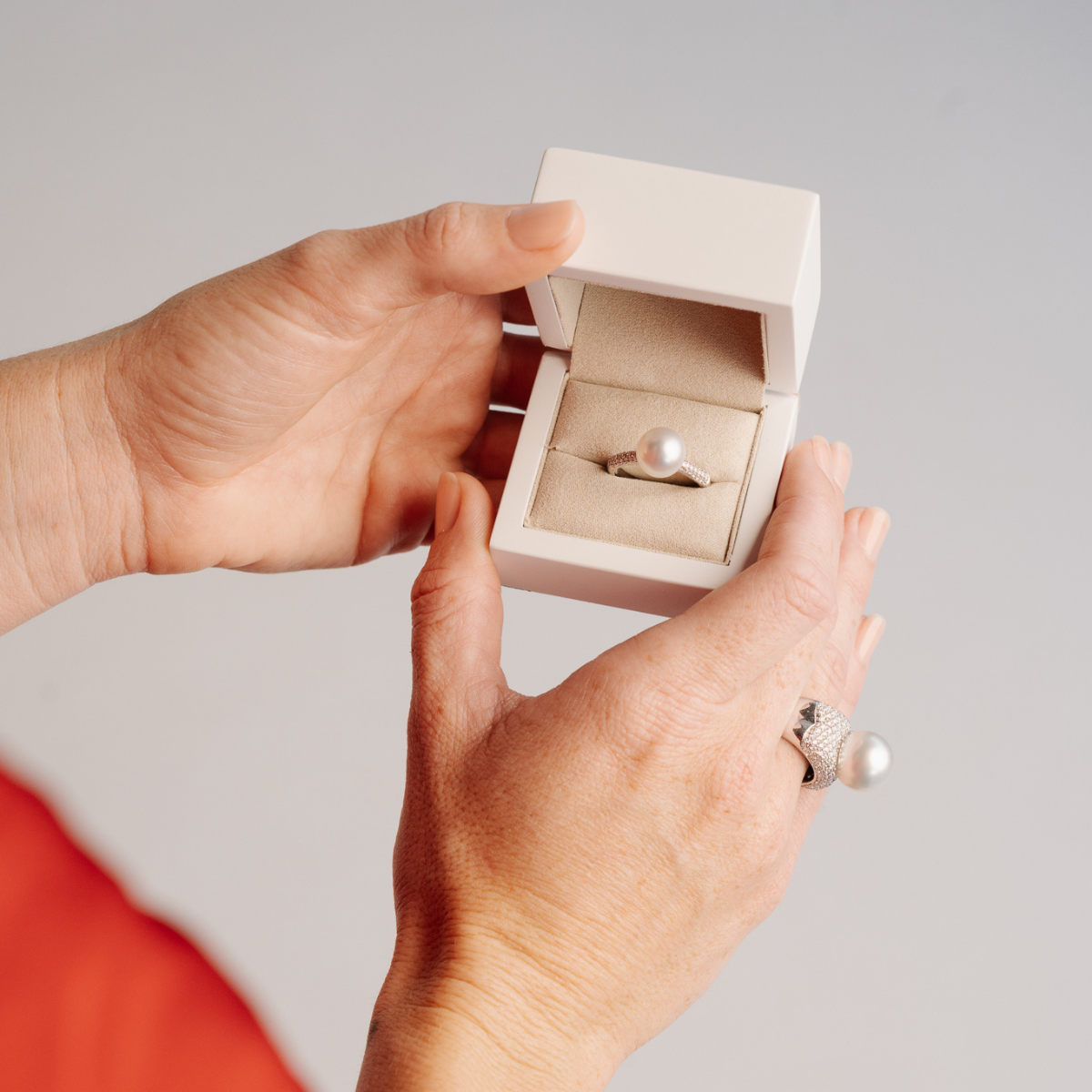 Person holding a white box with a pearl ring inside against a gray background