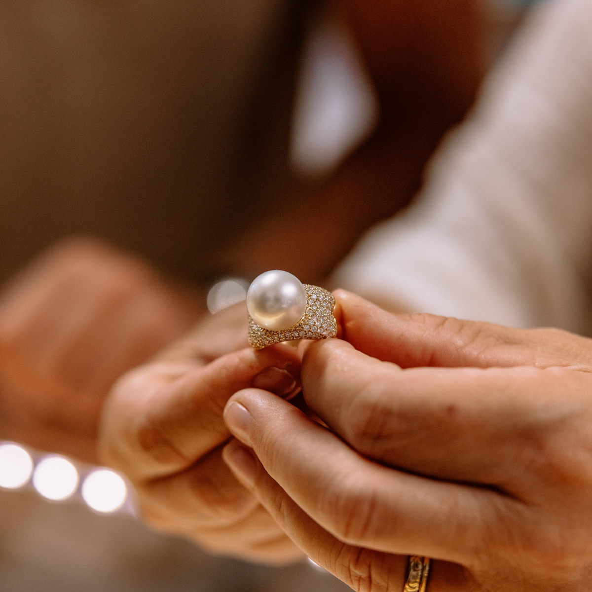 Close-up of hands holding a pearl ring with a blurred background