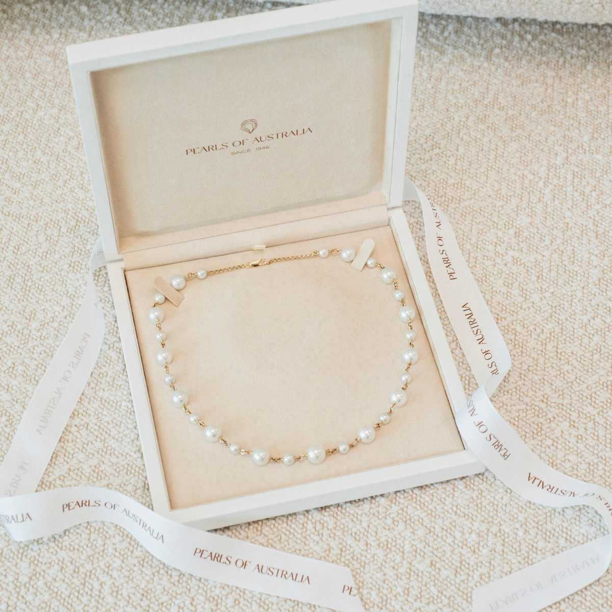 Pearl chain necklace in a 'Pearls of Australia' strand box on a textured surface.
