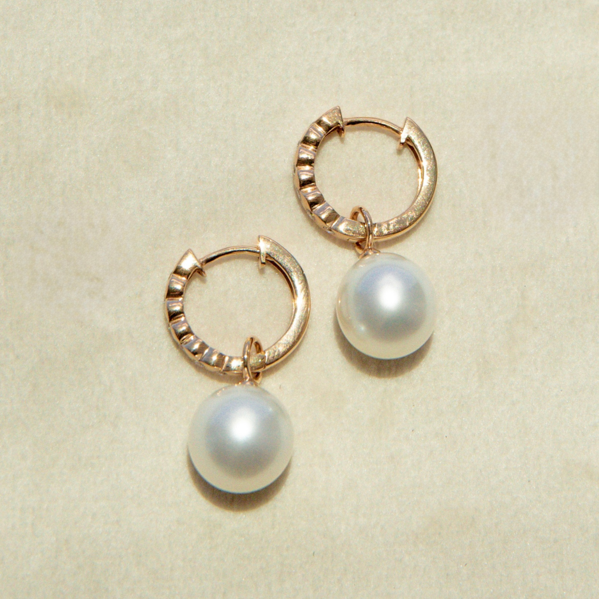 Gold hoop earrings with pearl drops on a beige background