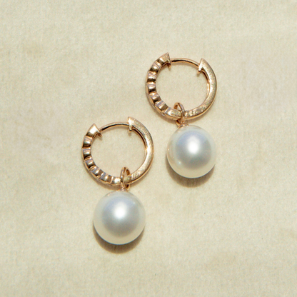 Gold hoop earrings with pearl drops on a beige background