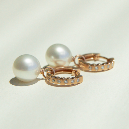 Two pearl earrings with rose gold and diamond accents on a light background