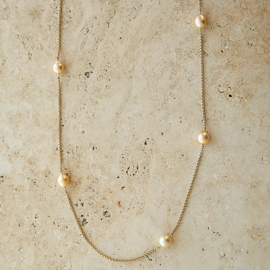 Gold chain necklace with gold pearls on a textured beige surface
