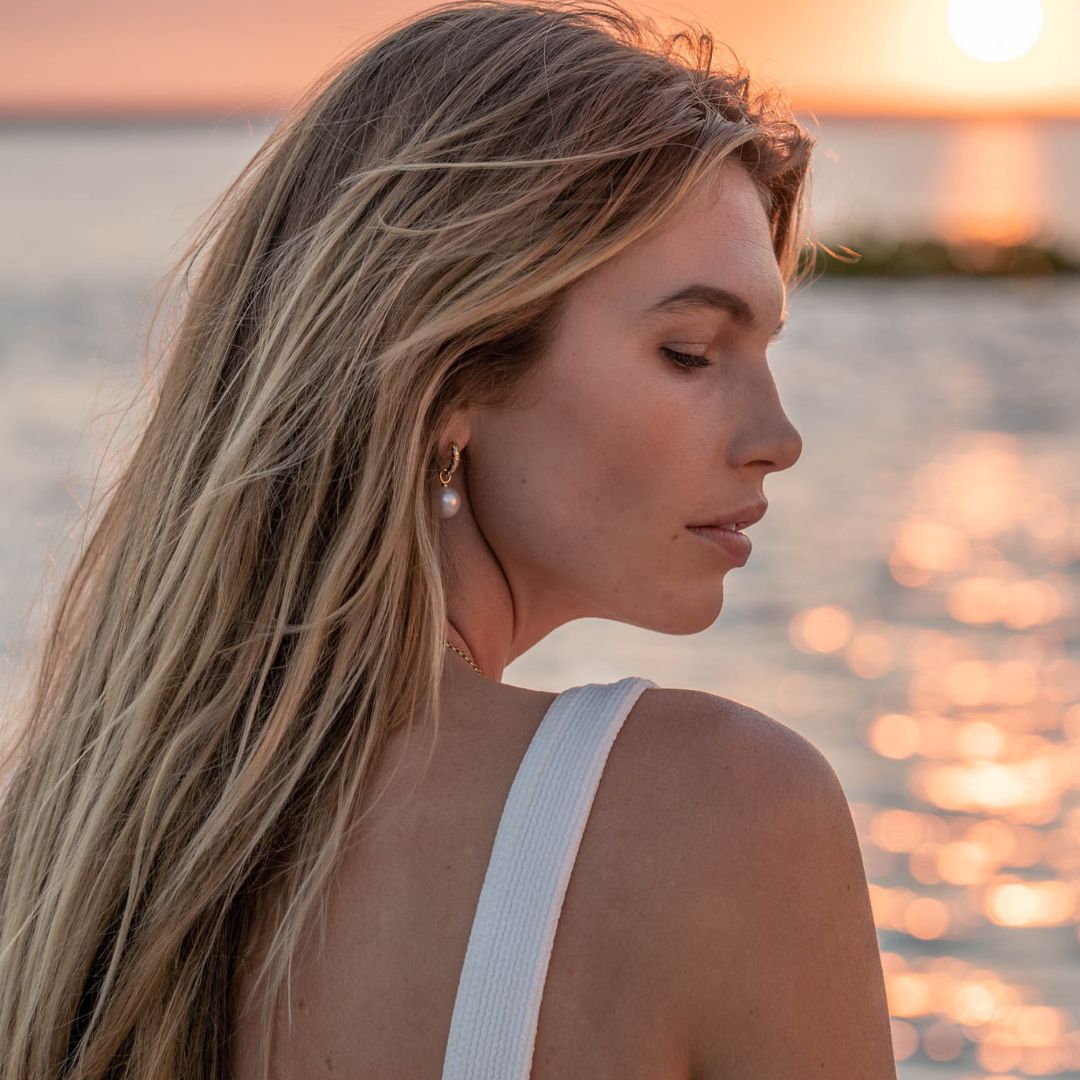 A woman wears her beautiful Cocos Pearl Huggies that feature round, white Australian South Sea pearls set in gold with sparkling white diamonds.