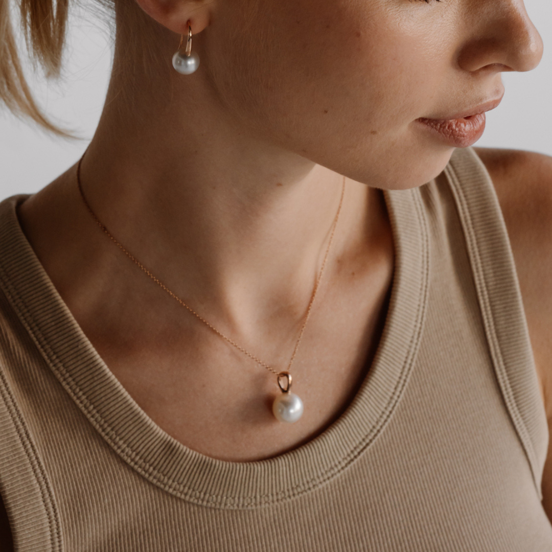 A woman wears her the beautiful Australian South Sea Cocos Pendant featuring a stunning round, white pearl set in gold. 