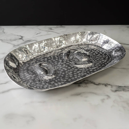 Decorative silver platter with crab design on a marble surface.