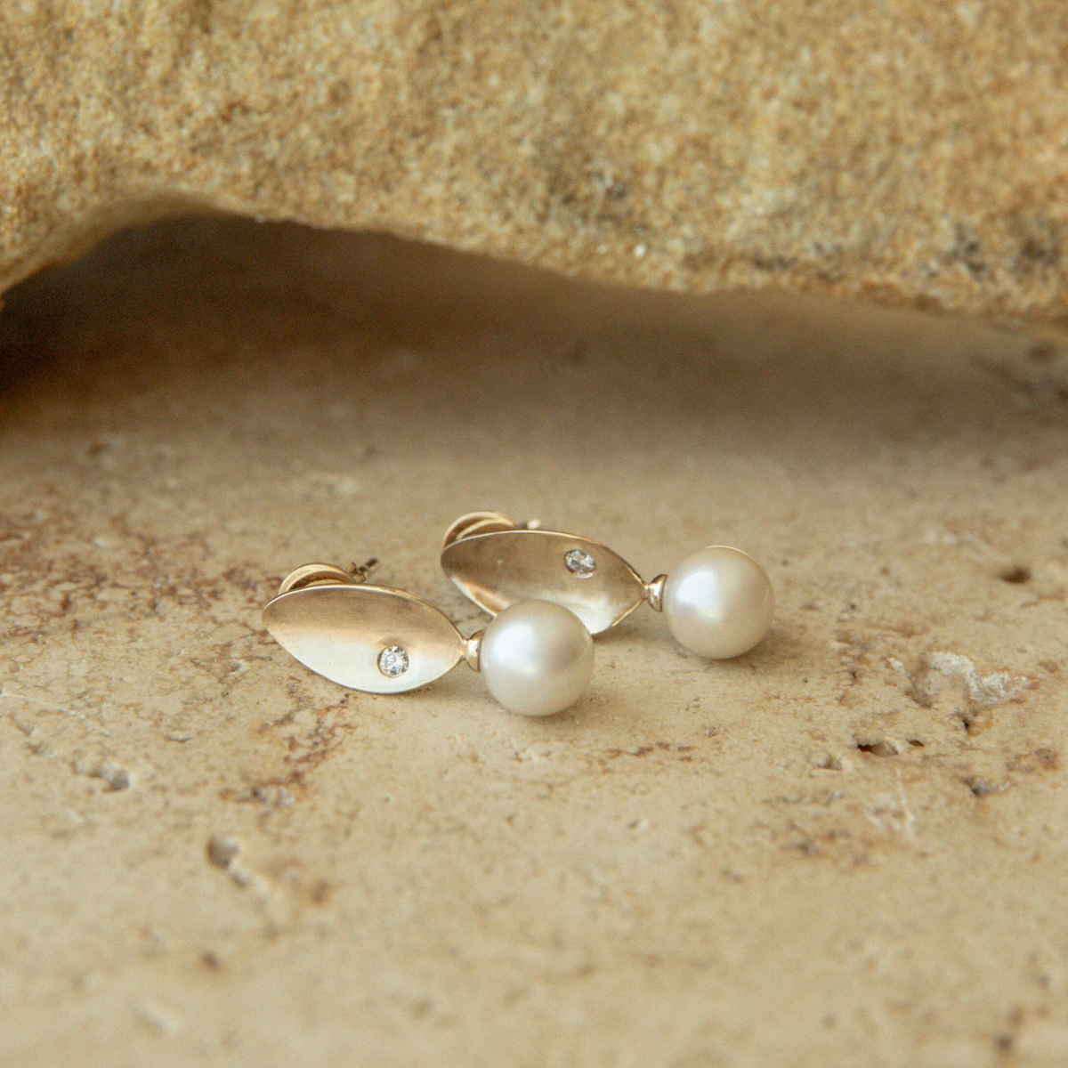 Pair of gold and pearl earrings on a textured beige surface