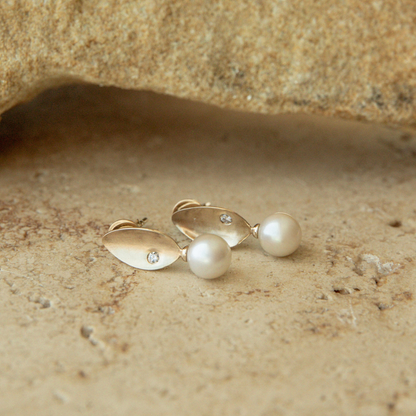 Pair of gold and pearl earrings on a textured beige surface