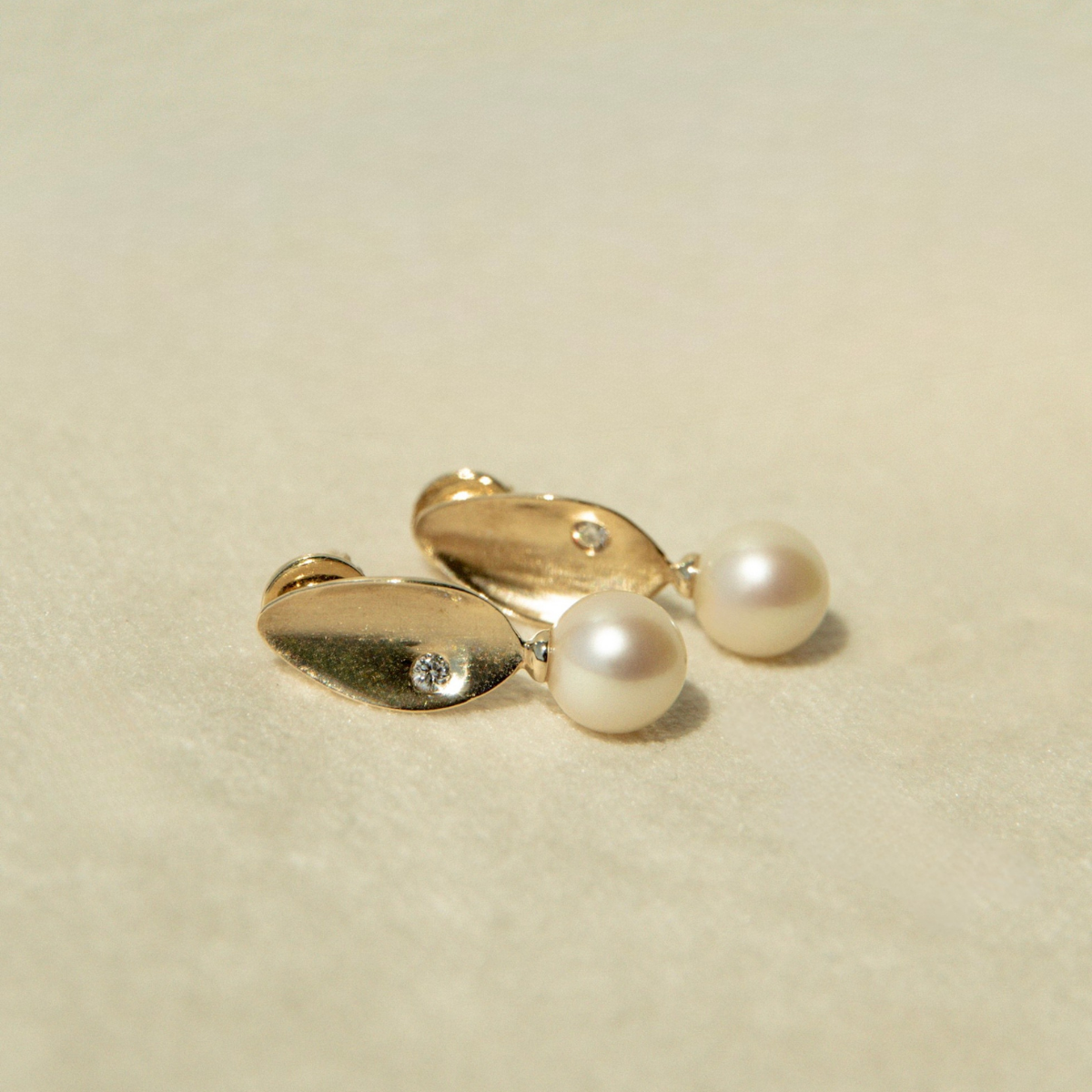 Pair of gold earrings with pearls on a beige background