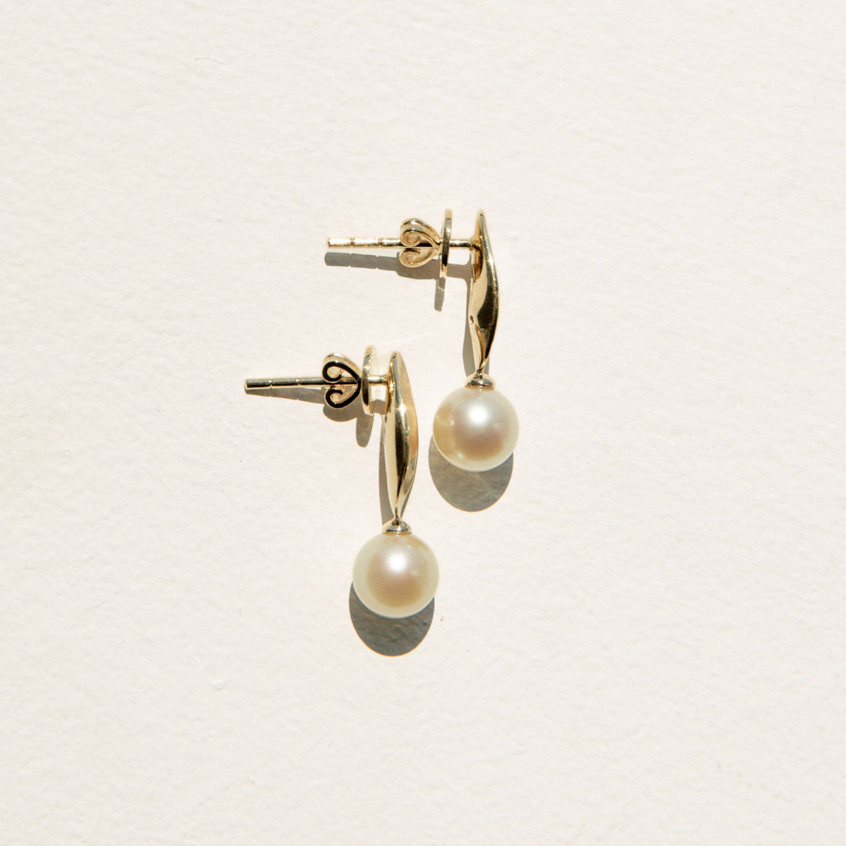Gold earrings with pearl drops on a light beige background