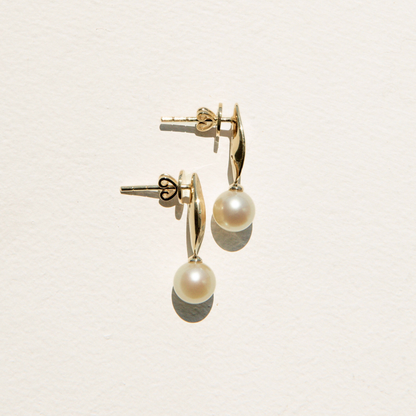 Gold earrings with pearl drops on a light beige background
