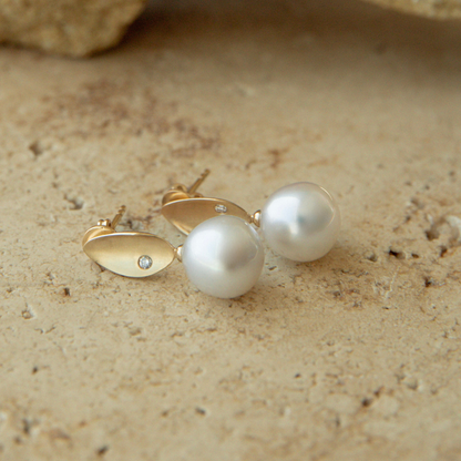 Pearl earrings with gold accents on a textured beige surface