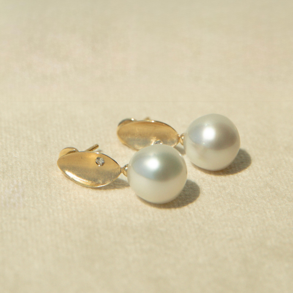 Pair of pearl earrings with gold clasps on a beige background