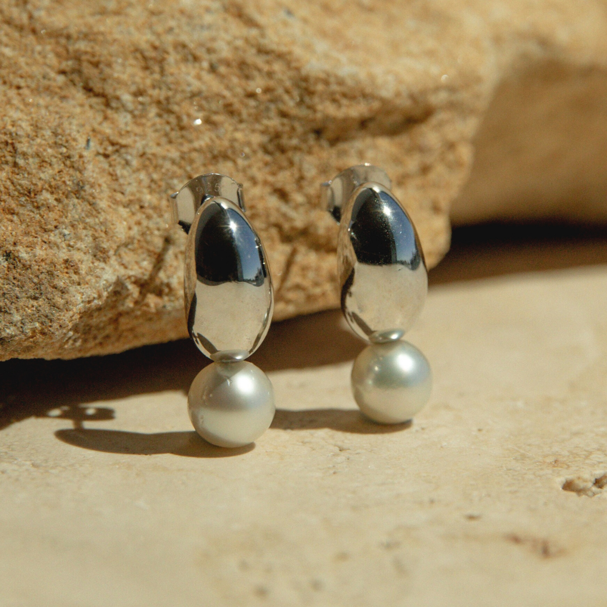 Silver earrings with pearls on a sandy surface