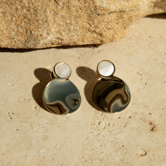 Pair of earrings on a sandy surface with a rock in the background