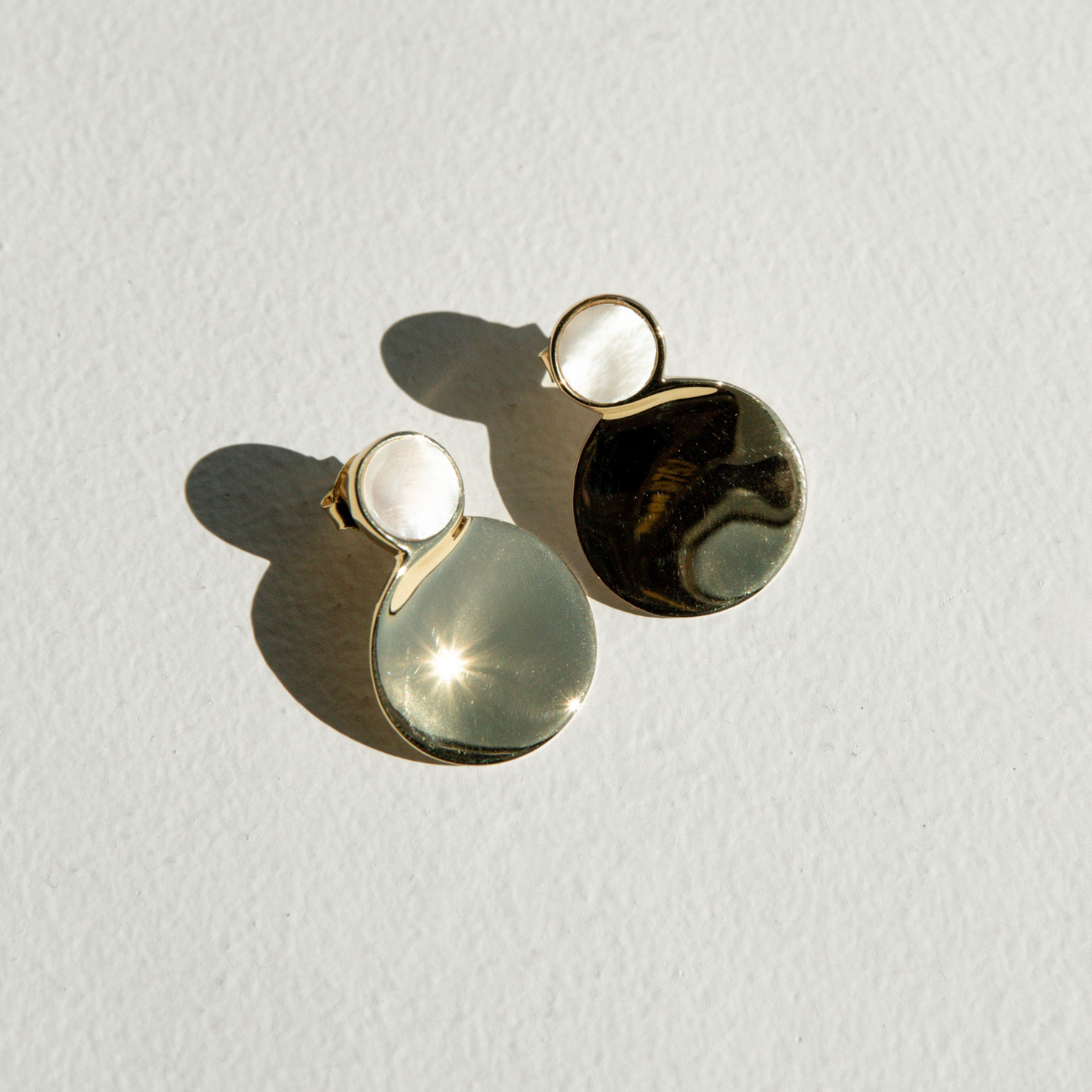 Pair of earrings with gold and mother of pearl components on a light gray background